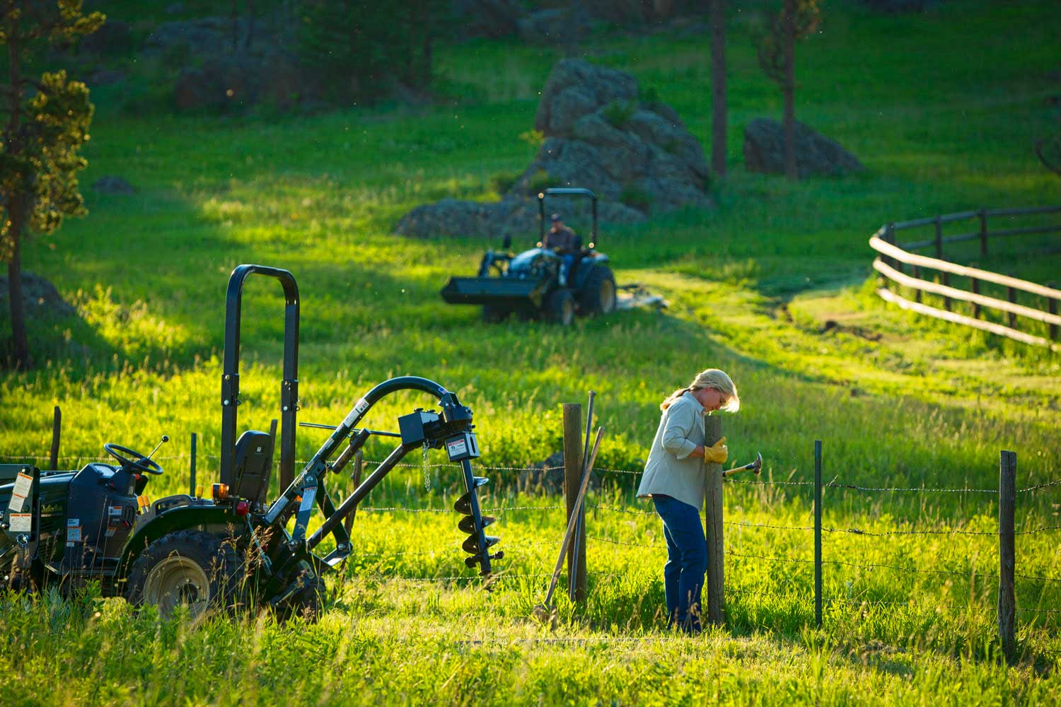 female-farmer-fixing-fence-post-with-auger